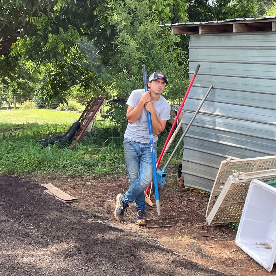 Mikey Floyd leaning on a rake beside the tool shed, squinting into the middle distance like a man who has seen weeds and defeated them